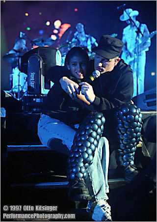 Live U2 concert photo of Bono w fan (fg), Larry Mullen Jr, Adam Clayton, The Edge (bg)